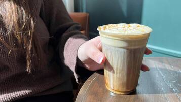 Una persona sosteniendo una taza de café con arte de latte sobre una mesa de madera.