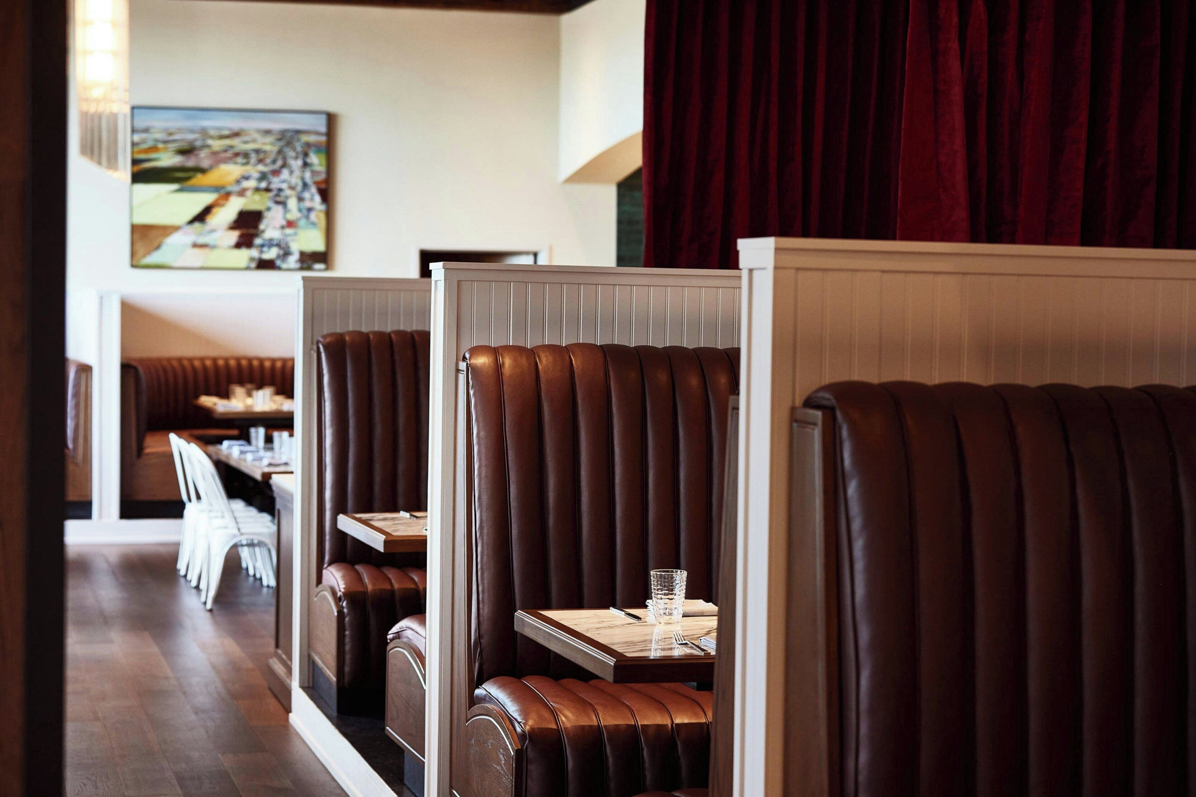 A restaurant with booth seating, a dining area, and a painting on the wall.