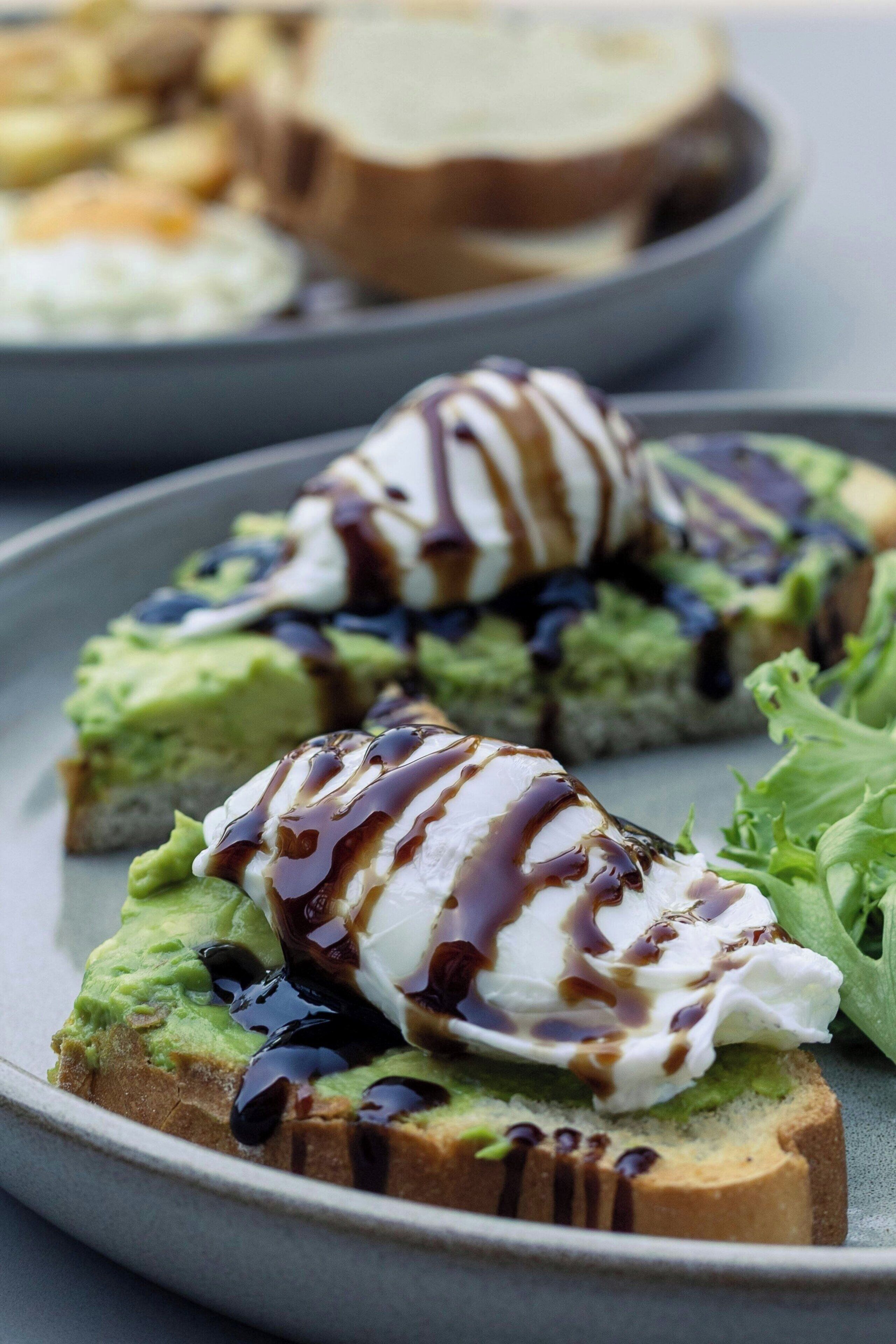 Un plato con tostada de aguacate, un huevo pochado encima y salsa por encima.