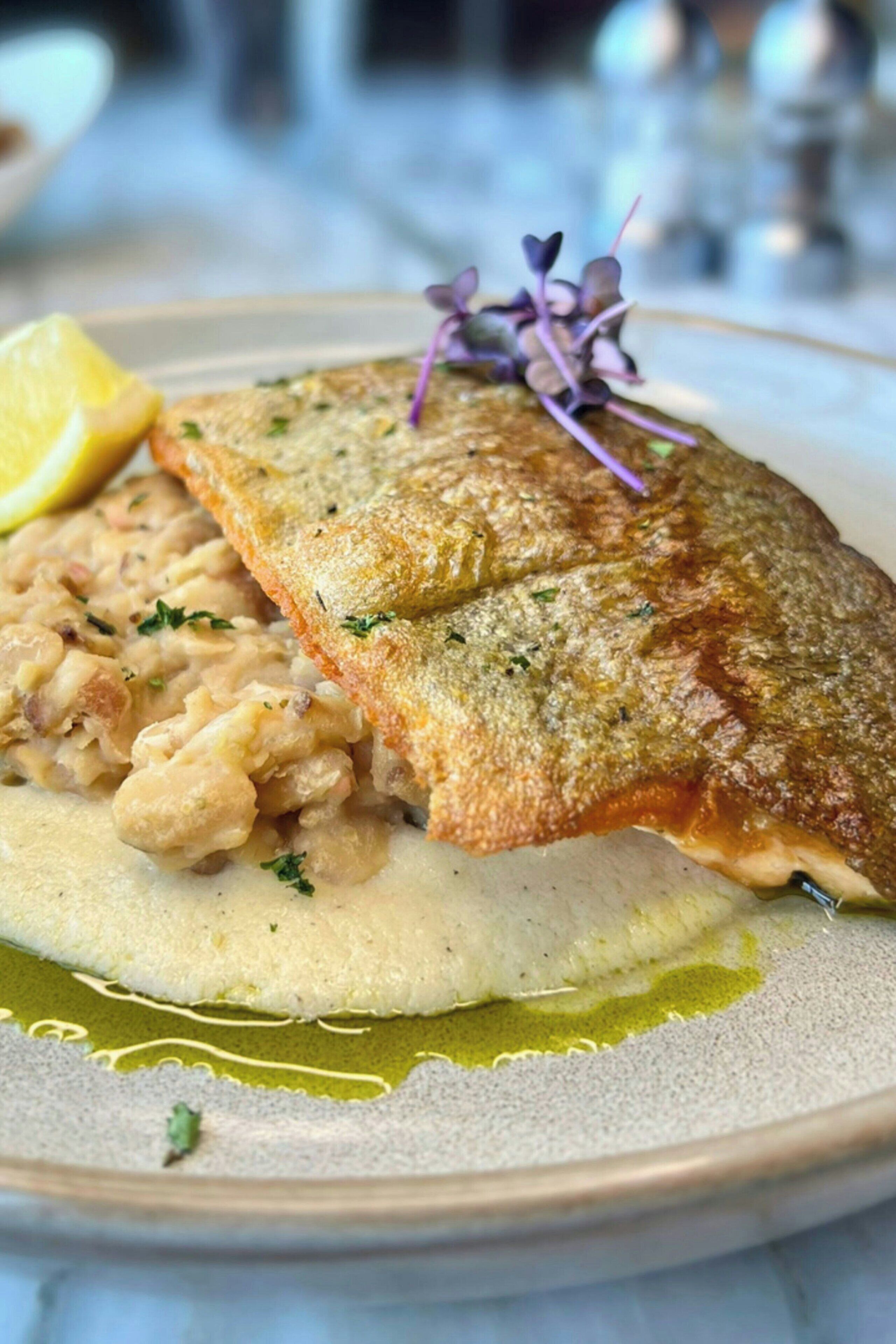 Ein Teller mit Fisch, Kartoffelpüree und einem Zitronenschnitz.