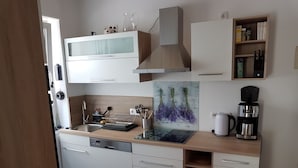 Eine moderne Küche mit weißen Schränken, einer Edelstahl-Dunstabzugshaube, einer Kaffeemaschine und einer Spritzschutze mit Lavendel-Design.