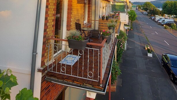 Ein Wohngebäude mit Backsteinfassade, einem Balkon mit Gartenmöbeln und Straßenansicht mit parkenden Autos.
