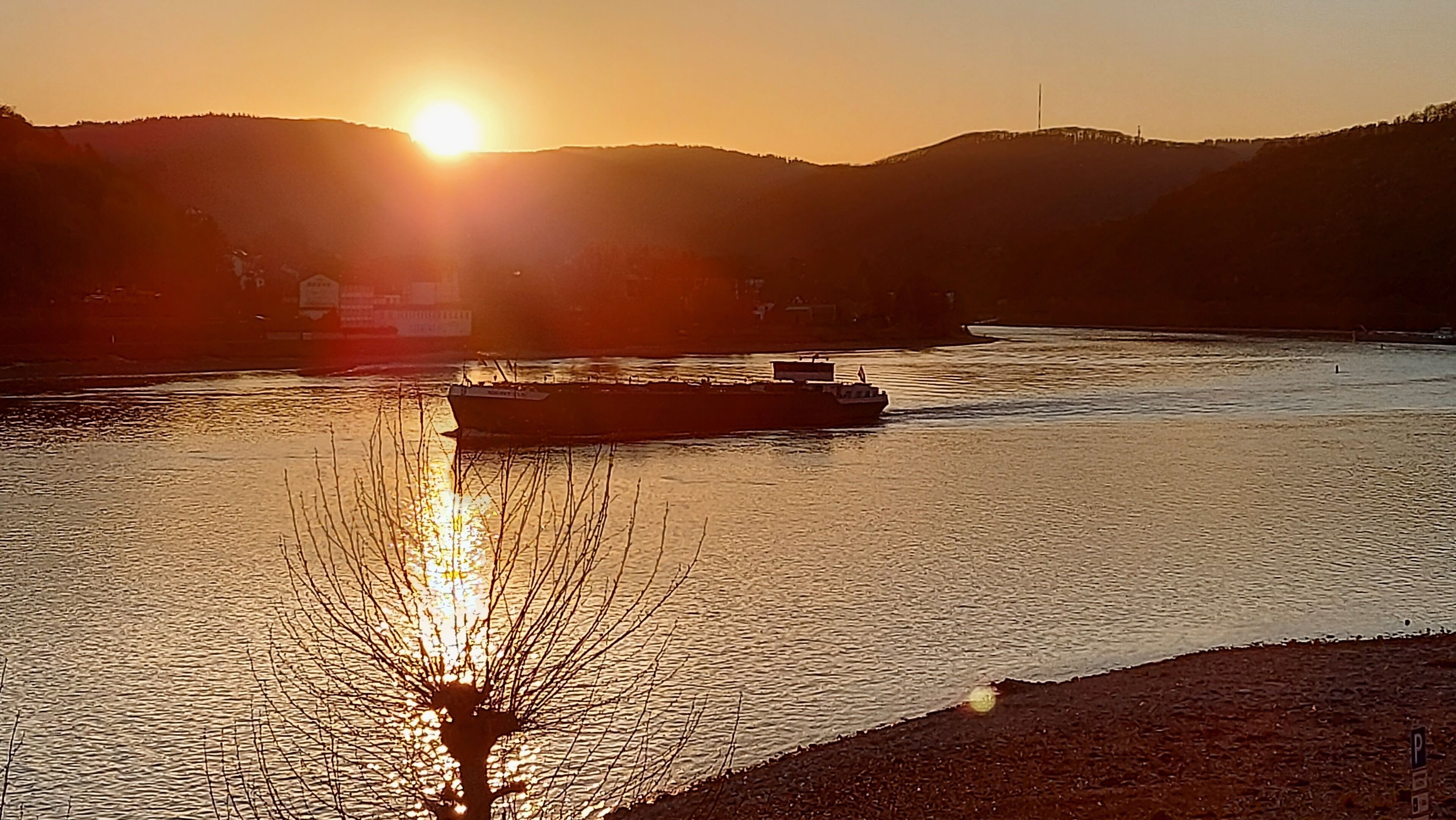 A sunset over a river with a boat and distant hills.