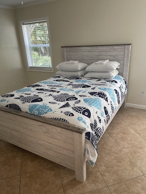 A bed with a patterned bedspread, a wooden headboard, and a window with blinds. - Port Salarno (Stuart)