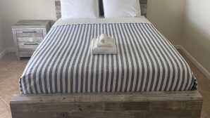 Ein Bett mit gestreifter Bettdecke, einem Holz-Kopfteil und drei gerahmten Bildern darüber.