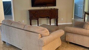 Ein Wohnzimmer mit beigefarbenen Sofas, einem Holztisch, einem Flachbildfernseher und einem Deckenventilator.