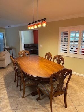 A dining room with a wooden table and chairs, a chandelier, and a window with blinds. - Port Salarno (Stuart)