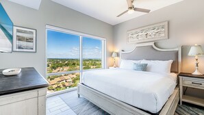 Un dormitorio con un ventanal grande, una cama, una mesita de noche y un ventilador de techo.