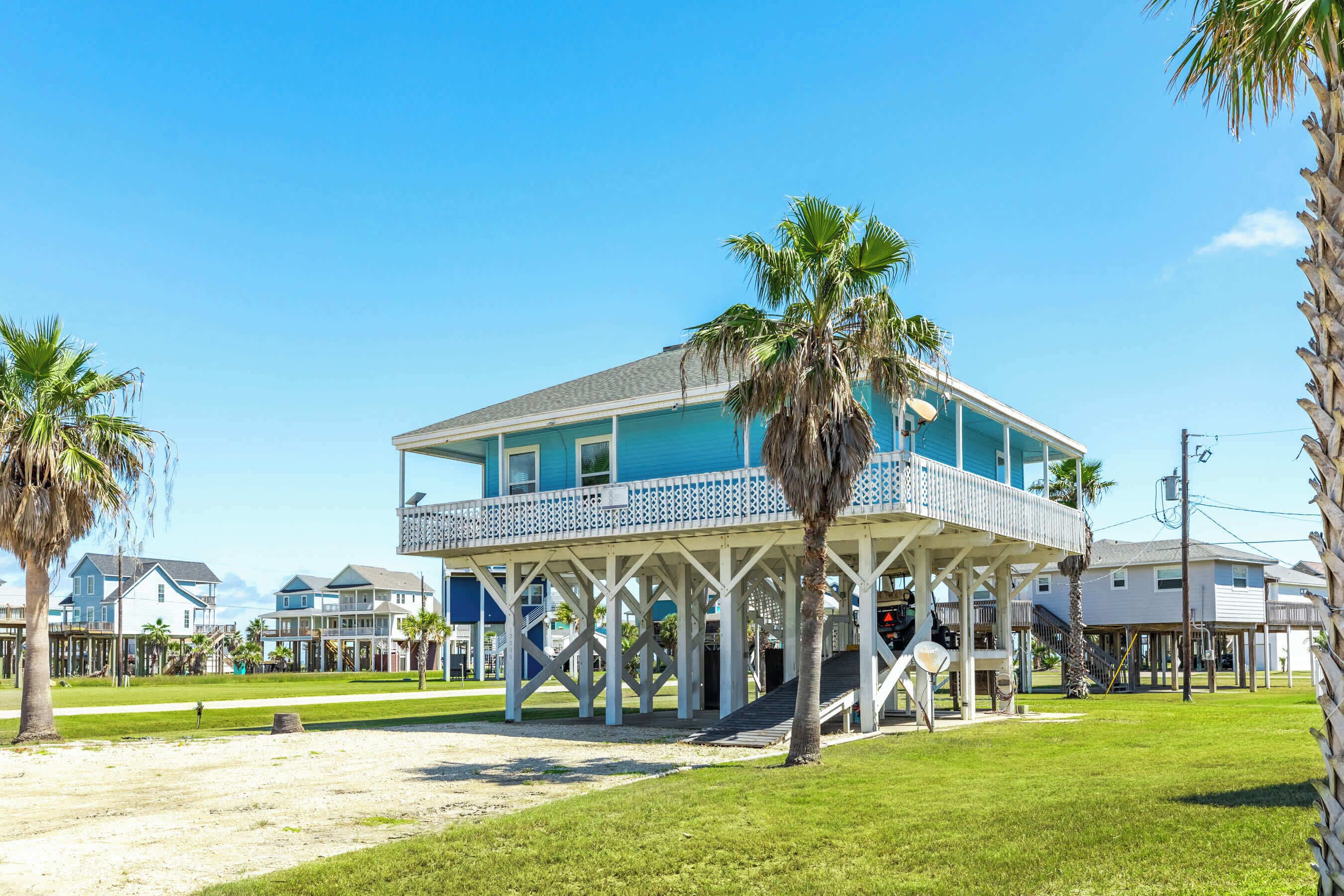 A beachfront house with a balcony, palm trees, and a clear sky.