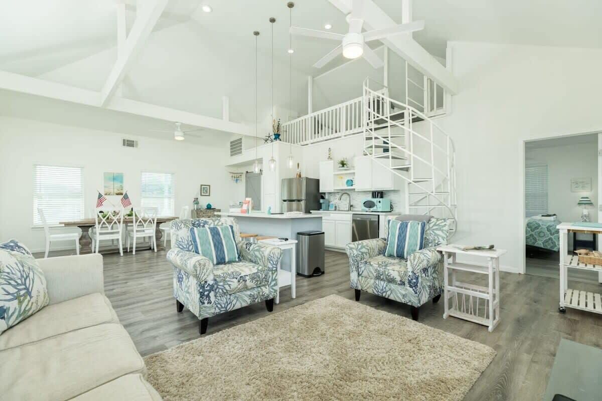 A spacious living area with a high ceiling, a staircase to an upper level, and a kitchen area.