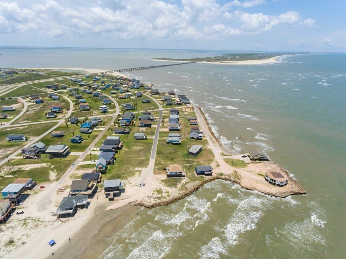 Vista aérea de una zona residencial costera con casas, una playa y un muelle.