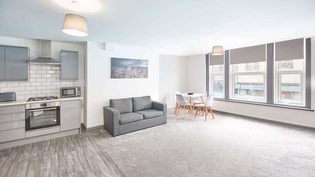 Una cocina moderna con sofá gris y comedor, ventanas amplias y vistas a la ciudad.