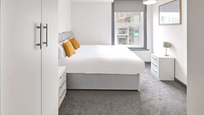 Un dormitorio moderno con una cama grande, un armario, una mesita de noche y una ventana con vistas a la ciudad.