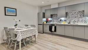Eine moderne Küche mit grauen Schränken, einer Fischgrät-Spritzwand und einem Essbereich mit Tisch für vier Personen.