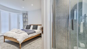 Ein Schlafzimmer mit Bett, Duschkabine und einem Fenster mit Jalousien.