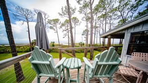 Een houten terras met twee Adirondack stoelen en een tafel, met uitzicht op een strand en de oceaan.