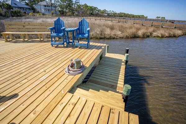 A wooden deck with a bench and three blue Adirondack chairs.