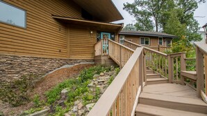 A wooden house with a stone foundation, a wooden staircase, and a small adjacent building. - Big Hilltop Home with Gorgeous Lake Views & Beach Access (Michigan City)