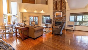 A spacious living room with a fireplace, wooden flooring, and a stone accent wall. - Big Hilltop Home with Gorgeous Lake Views & Beach Access (Michigan City)