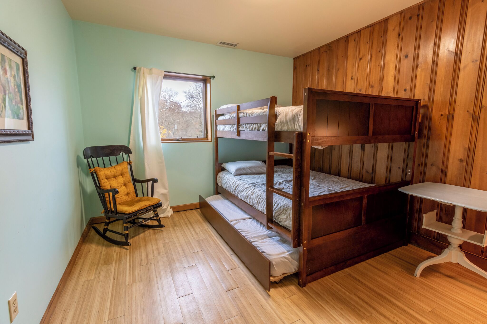 A bunk bed room with a rocking chair and a small table.