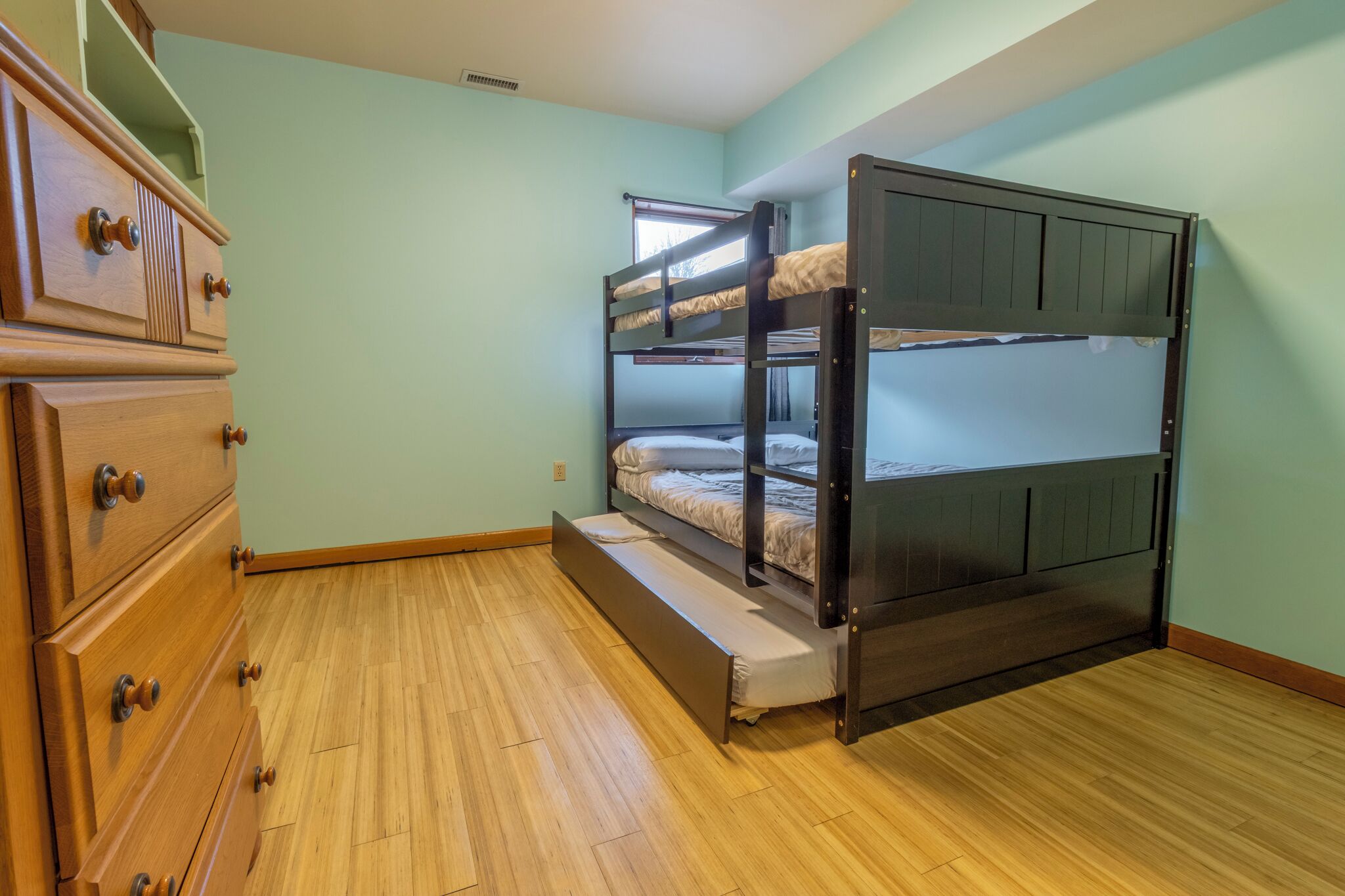 A room with a bunk bed, wooden dresser, and a window.