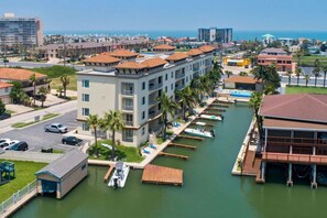 A marina with docked boats, a building with balconies, and a view of the ocean. - Las Marinas #202 | Waterfront Condo • Boat Slip • 6 Minute Walk to Beach (South Padre Island)