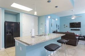 A modern kitchen with granite countertops, a black refrigerator, and a bar area with stools.