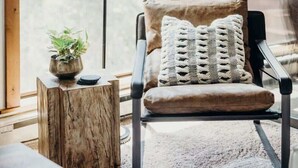 A cozy room with a large window, a floor lamp, a chair with cushions, a small wooden table, and a potted plant. - Prime Location | Luxurious Condo | Near Main St (Breckenridge)