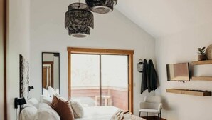 A bedroom with a bed, a large window, a TV, and a hanging light fixture. - Prime Location | Luxurious Condo | Near Main St (Breckenridge)