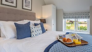 Ein ordentlich bezogenes Bett mit einer Eiergebäckplatte und Orangensaft, ein gerahmtes Bild darüber und ein Fenster mit Blick auf Grünflächen.