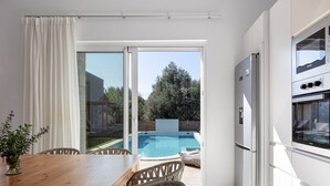 A modern kitchen with a built-in oven and refrigerator, a wooden dining table with wicker chairs, and a glass door leading to a swimming pool. - Mandana Villa - With Private Pool & Jacuzzi (Pigi)