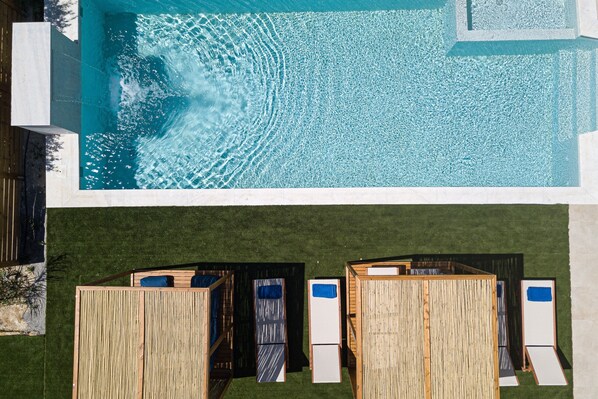 A swimming pool with clear water and a wooden deck area with lounge chairs.