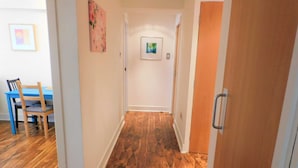 A hallway with wooden flooring, a dining table with chairs, and a door with a handle.