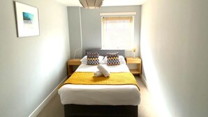 A bedroom with a bed, a hanging light fixture, a window with blinds, and a framed picture on the wall.