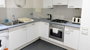 A kitchen with white cabinets, a stainless steel sink, a kettle, a toaster, and an oven.