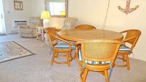 A dining area with a round wooden table and wicker chairs, a beige sofa, a lamp, and a decorative anchor on the wall. - Barefoot Country 304 1 Bedroom Condo by RedAwning (Ocean City)