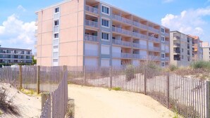 A multi-story building with balconies, a sandy path leading to the entrance, and a wooden fence. - Barefoot Country 304 1 Bedroom Condo by RedAwning (Ocean City)