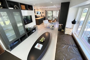 A modern living room with a black sofa, a glass coffee table, and a dining area with a round table and chairs.