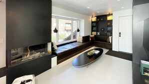 En moderne stue med pejs, en sort sofa, et sofabord og en bogreol.