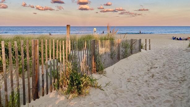 A beach with a wooden fence, sandy path, and a view of the ocean.
