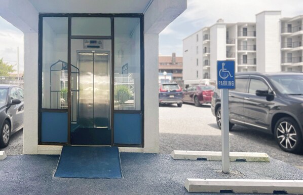 Ein Gebäudeeingang mit Glastür, einer Rampe und einem Parkschild für Behindertenparkplätze.