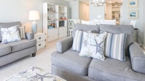 A living room with a grey sofa, a coffee table, and a lamp. There is a bookshelf in the background. - Direct ocean front  * 2 Bedrooms * 2 Full Baths + Den * 4th Floor Sleeps 8 * (Ocean City)