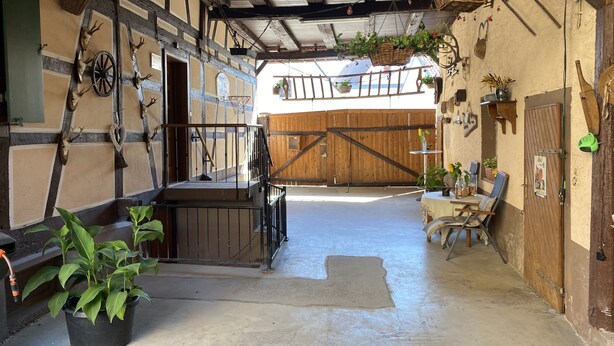 A rustic barn interior with a wooden staircase, hanging baskets, and a concrete floor. - s Moose Hof (Weisweil)