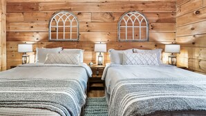 Quarto de cabana de madeira com duas camas, cada uma com mesa de cabeceira e abajur.