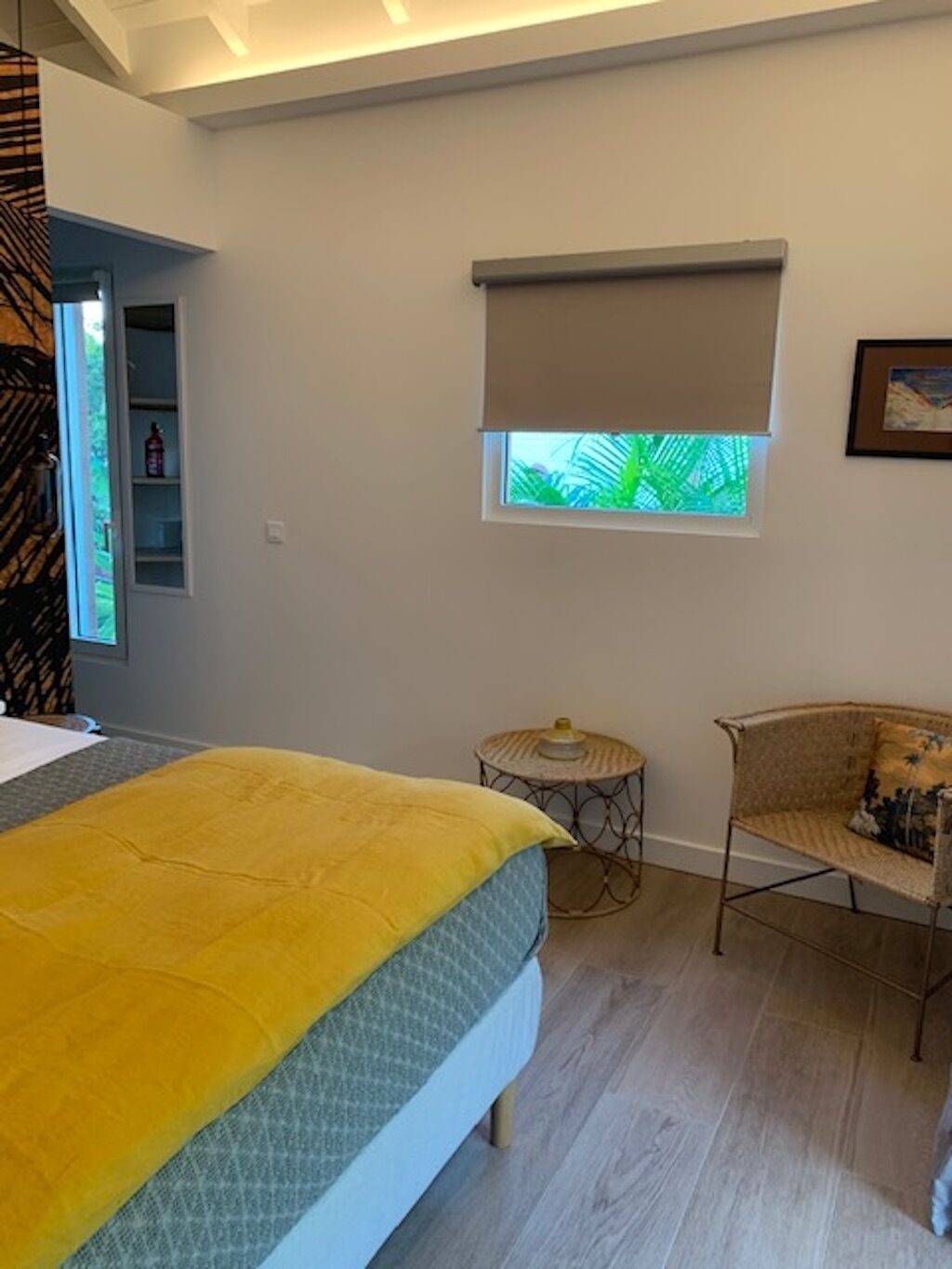 Une chambre avec un lit, une fenêtre donnant sur un paysage verdoyant, une petite table ronde et une chaise en osier.
