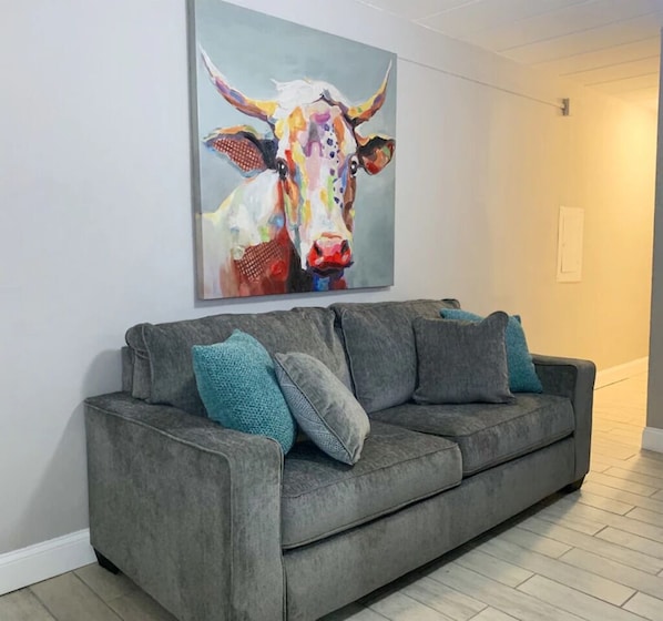 A grey sofa with teal cushions in a room with a large abstract painting of a bull on the wall.