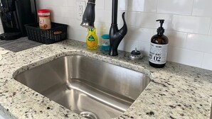 A kitchen with a stainless steel sink, a coffee maker, a bottle of dish soap, and a bottle of hand sanitizer. - Capital City Condo #3 (Frankfort)