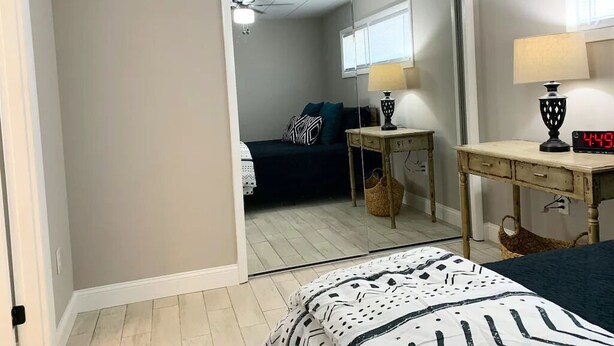 A bedroom with a bed, a bedside table with a lamp, a mirror, and a clock. - Capital City Condo #3 (Frankfort)