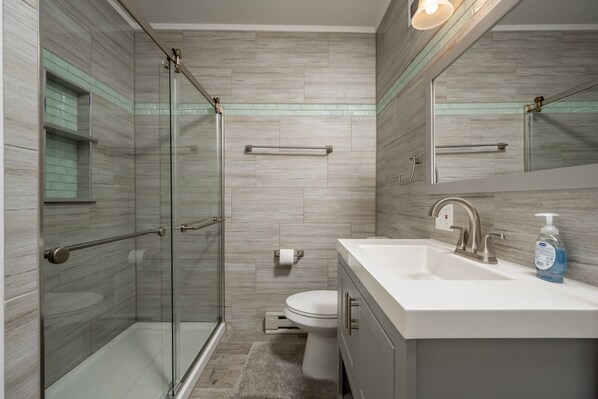 Un baño moderno con ducha de vidrio, inodoro y lavamanos con espejo.