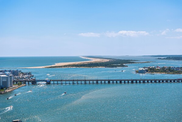 A coastal cityscape with a prominent pier extending into the sea, a sandy beach, and a clear blue sky.
